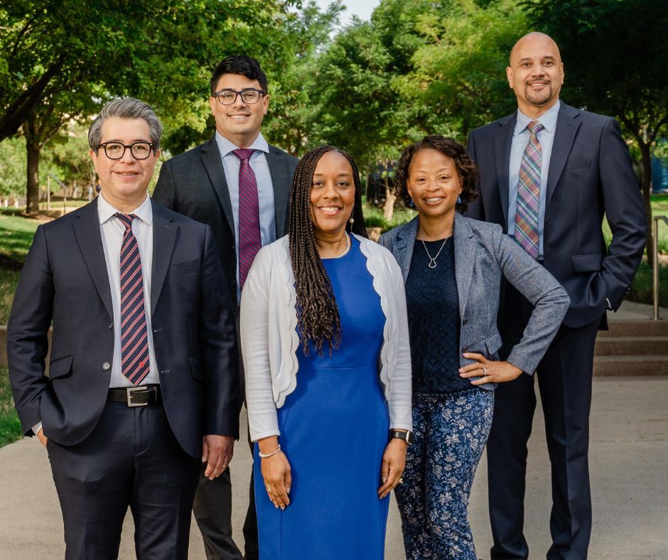 Three men and two women standing outdoors on a college campus